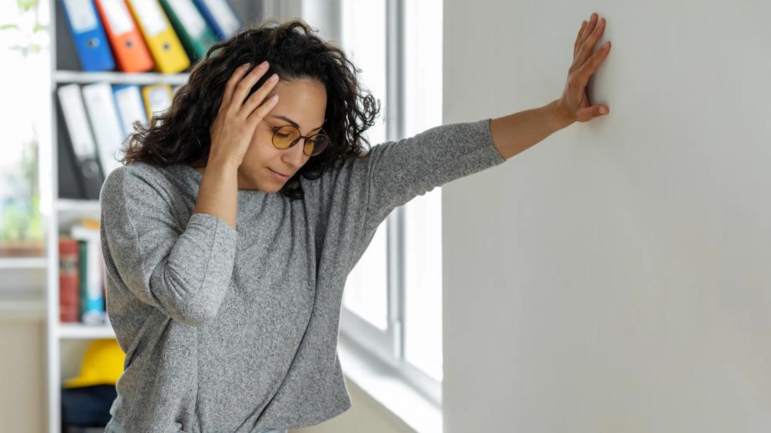 Person leaning against wall, holding their head