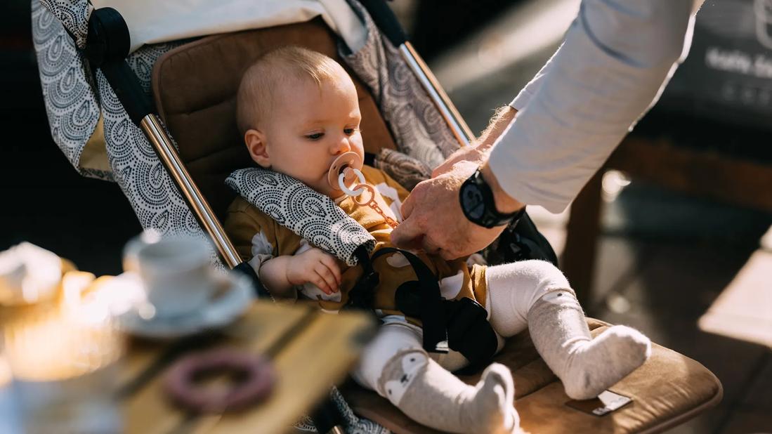 Baby with pacifier sitting in stroller, being strapped in