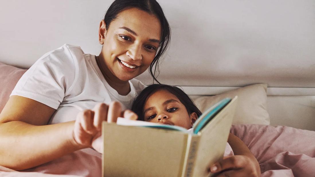 Smiling caregiver reading to child in bed