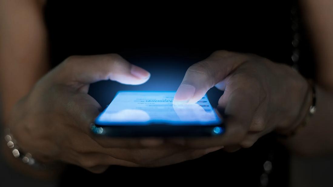 Hands holding cell phone, emitting blue light