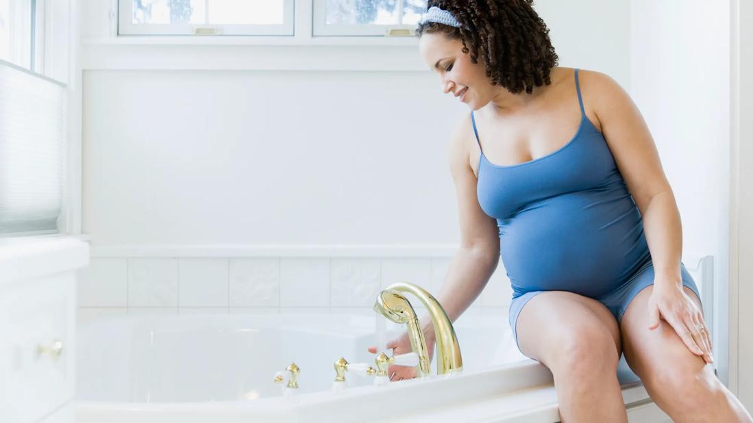 Pregnant woman drawing a bath and testing the temperature with her hand