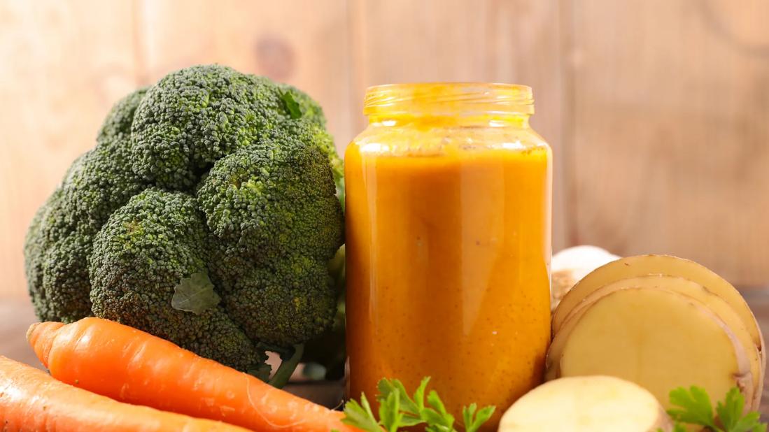Mason jar of pureed vegetables with broccoli, carrots and potatoes around it