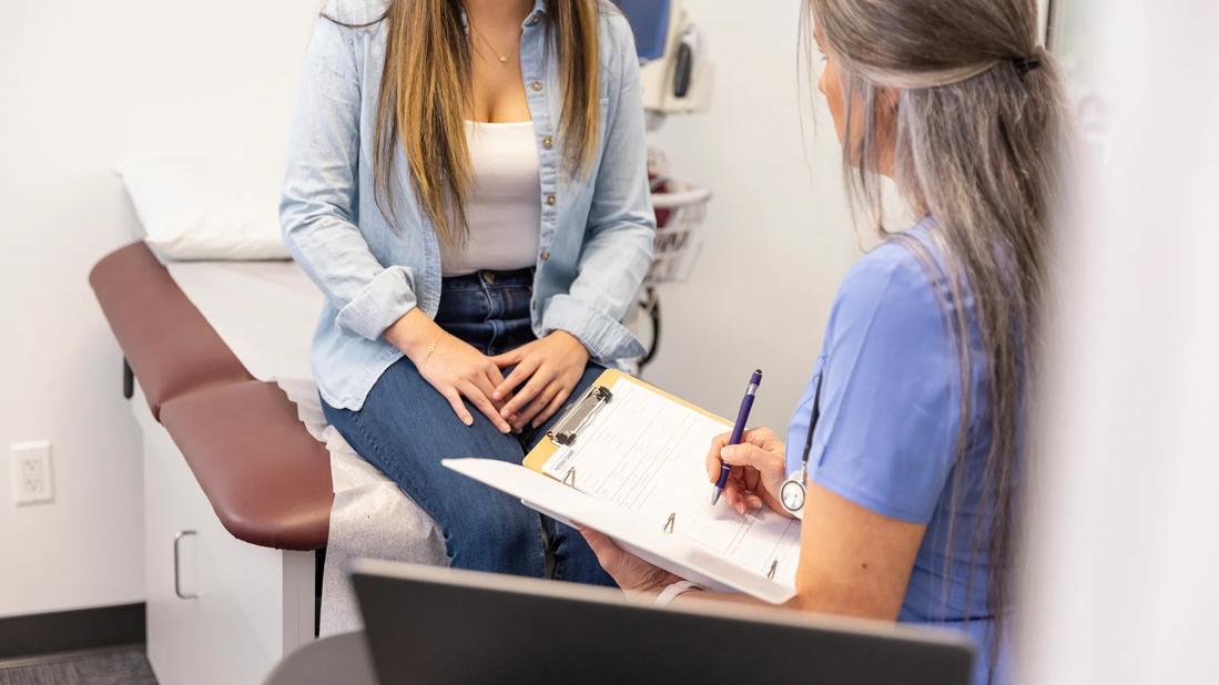 Female patient sitting on exam table discussing health with healthcare provider