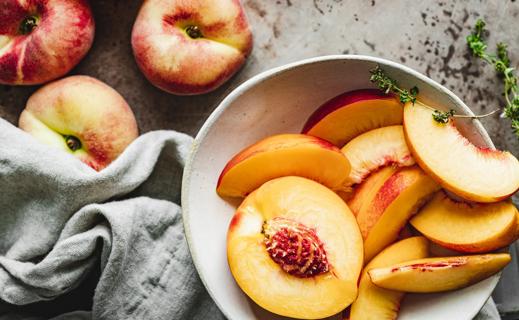 Bowl of sliced nectarines and whole nectarines on table with kitchen towel