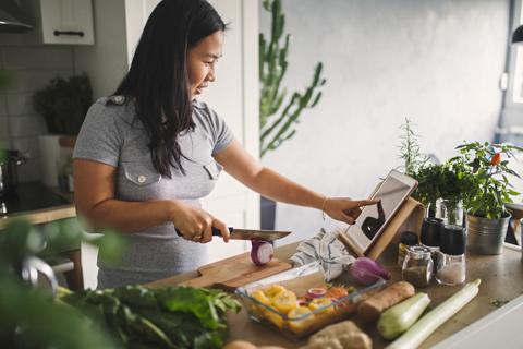 Person looking at a recipe on tablet in kitchen, using healthy, nutritional ingredients
