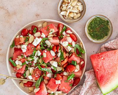 A bowl of watermelon salad with feta cheese, herbs and sliced almonds