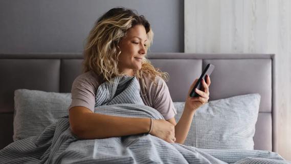 woman in bed looking at her phone and smiling